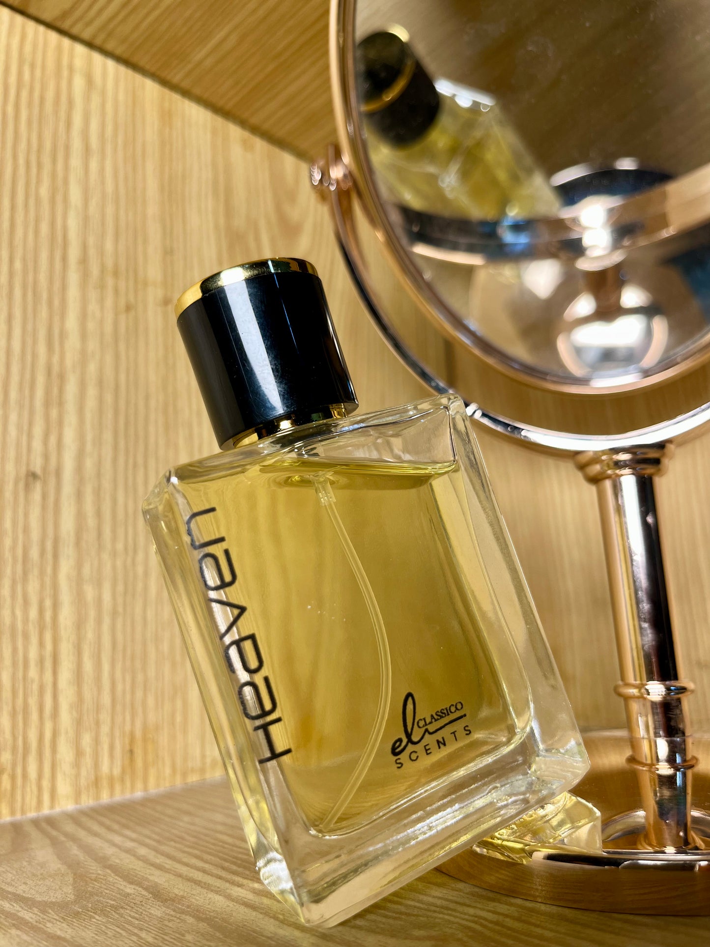 Perfume bottle labeled 'HEAVEN' by 'elusive scents' on a wooden surface with a mirror in the background.