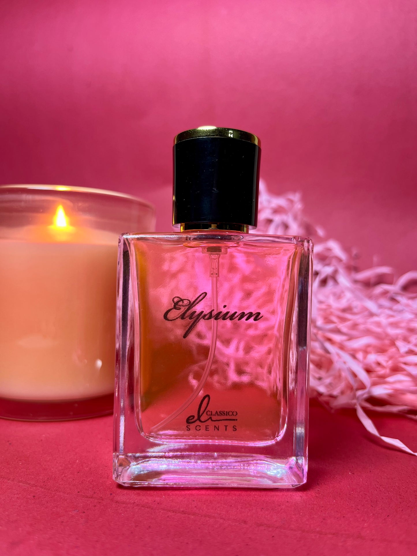 Perfume bottle labeled 'Elysium' next to a lit candle on a pink background