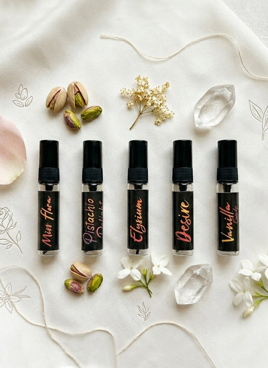 Five black perfume bottles with names on a decorative surface with flowers and crystals