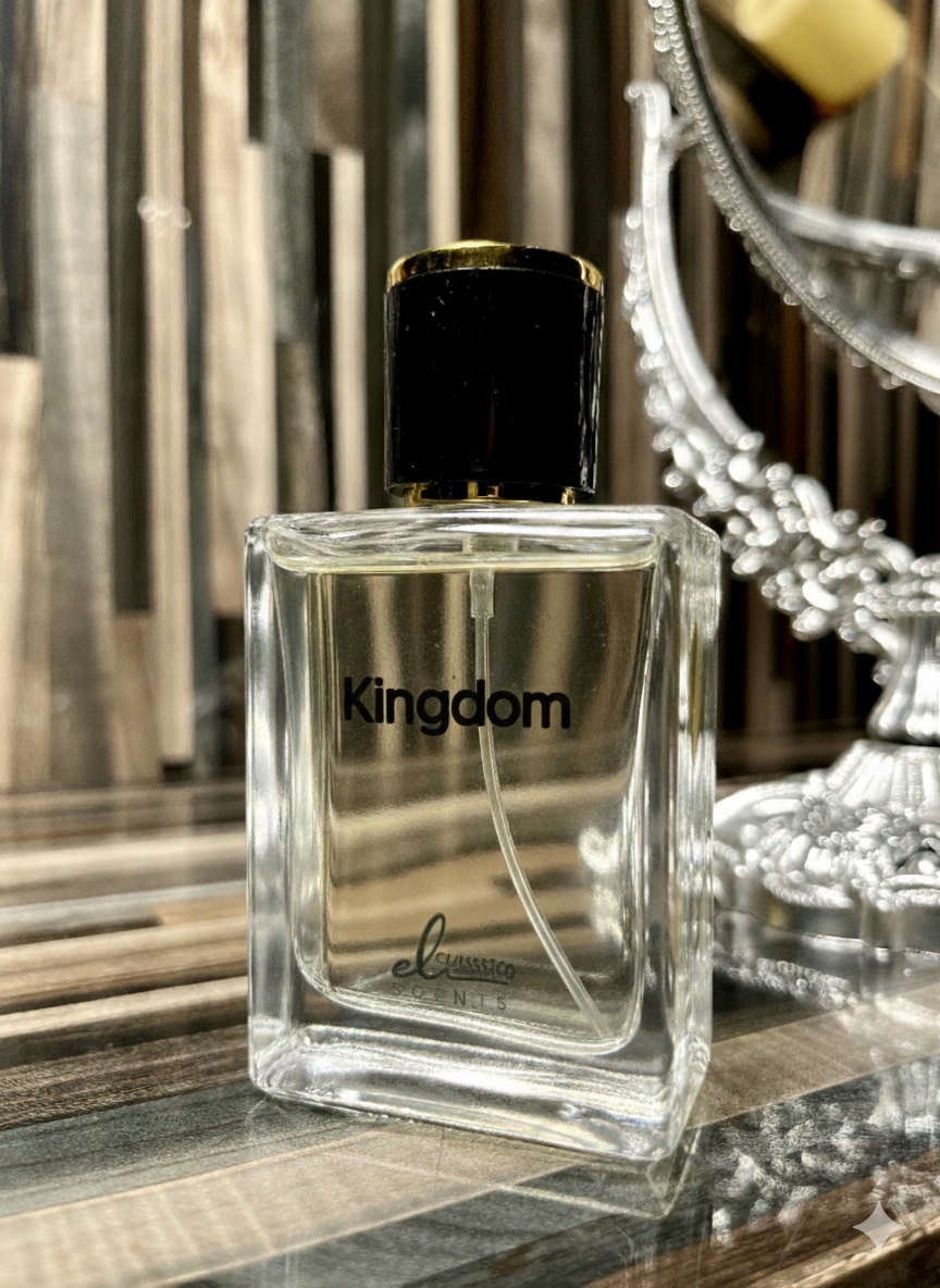 Clear perfume bottle labeled 'Kingdom' on a reflective surface with decorative elements.