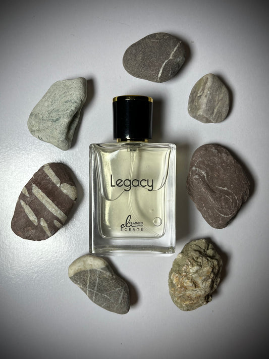 Perfume bottle labeled 'Legacy' surrounded by stones on a light gray background