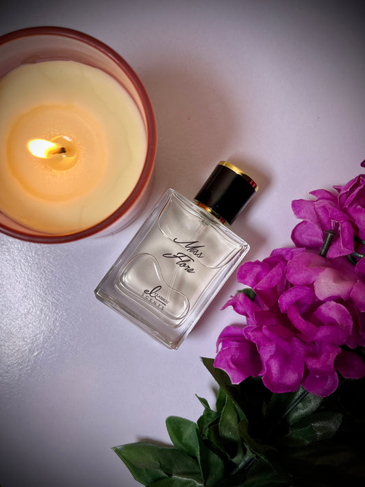 Perfume bottle with a lit candle and purple flowers on a reflective surface
