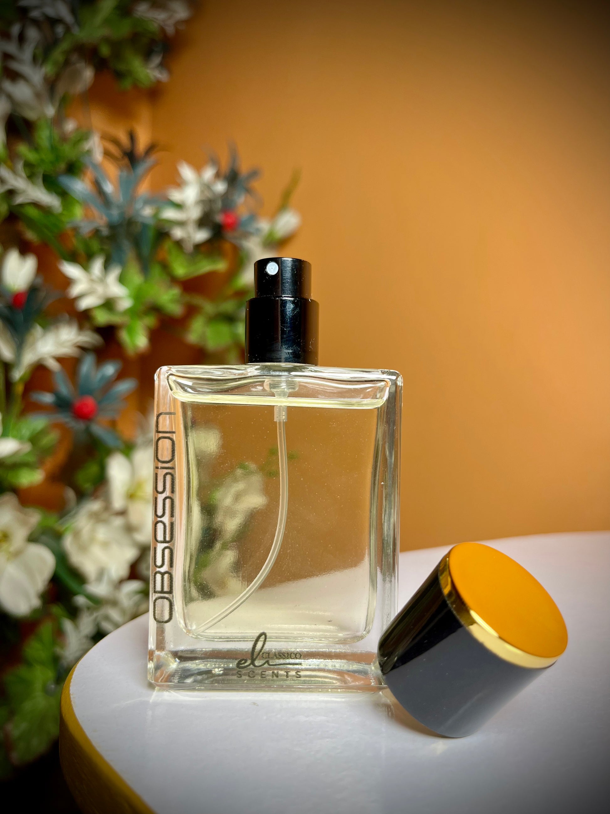 Perfume bottle labeled 'Obsession' on a surface with a blurred floral background